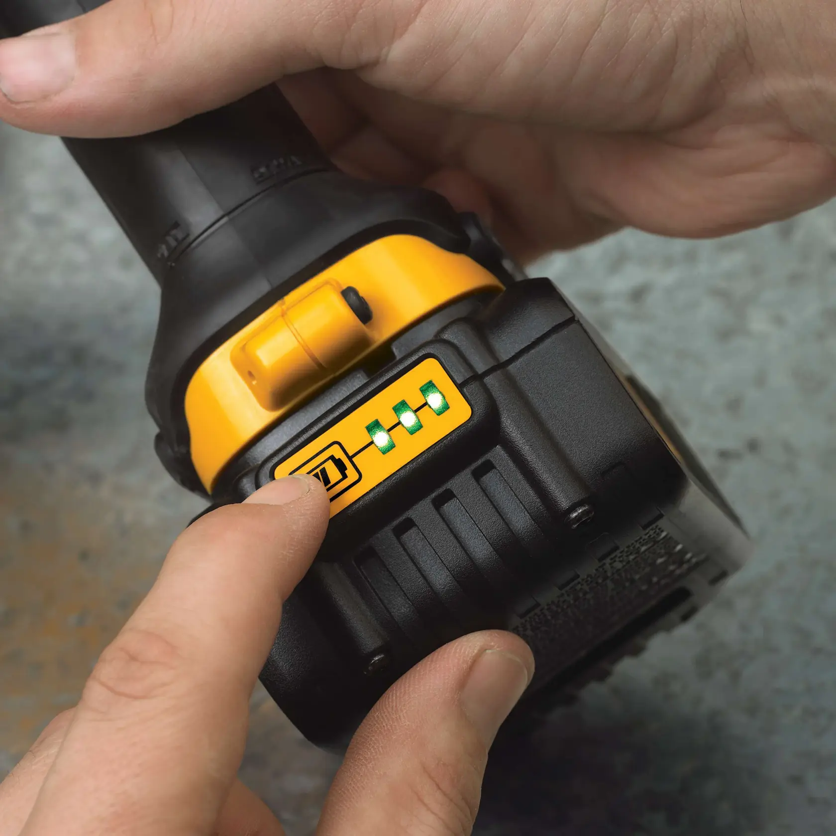 Vista en primer plano de una persona presionando el botón del indicador de batería en una herramienta eléctrica DEWALT. El indicador muestra tres luces verdes, lo que sugiere una alta carga de batería.