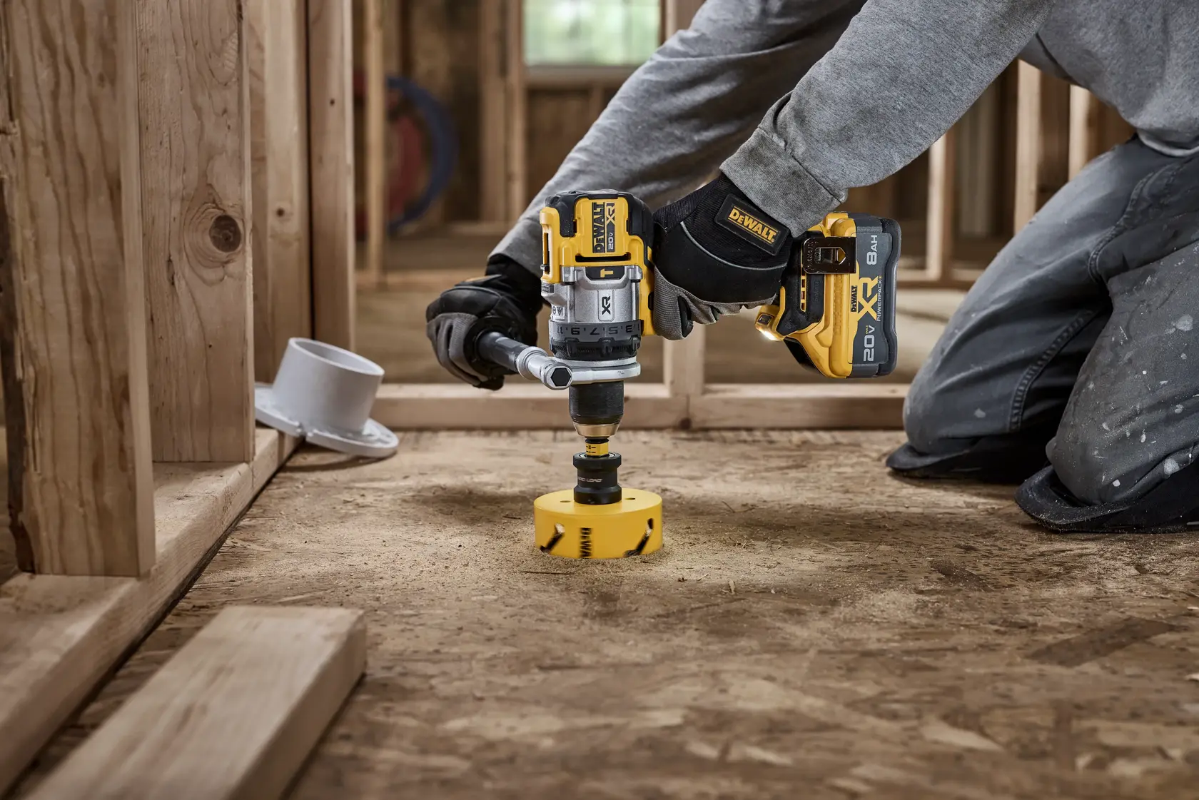 Persona usa taladro inalámbrico DEWALT con accesorio de sierra de corona en piso de madera en obra.