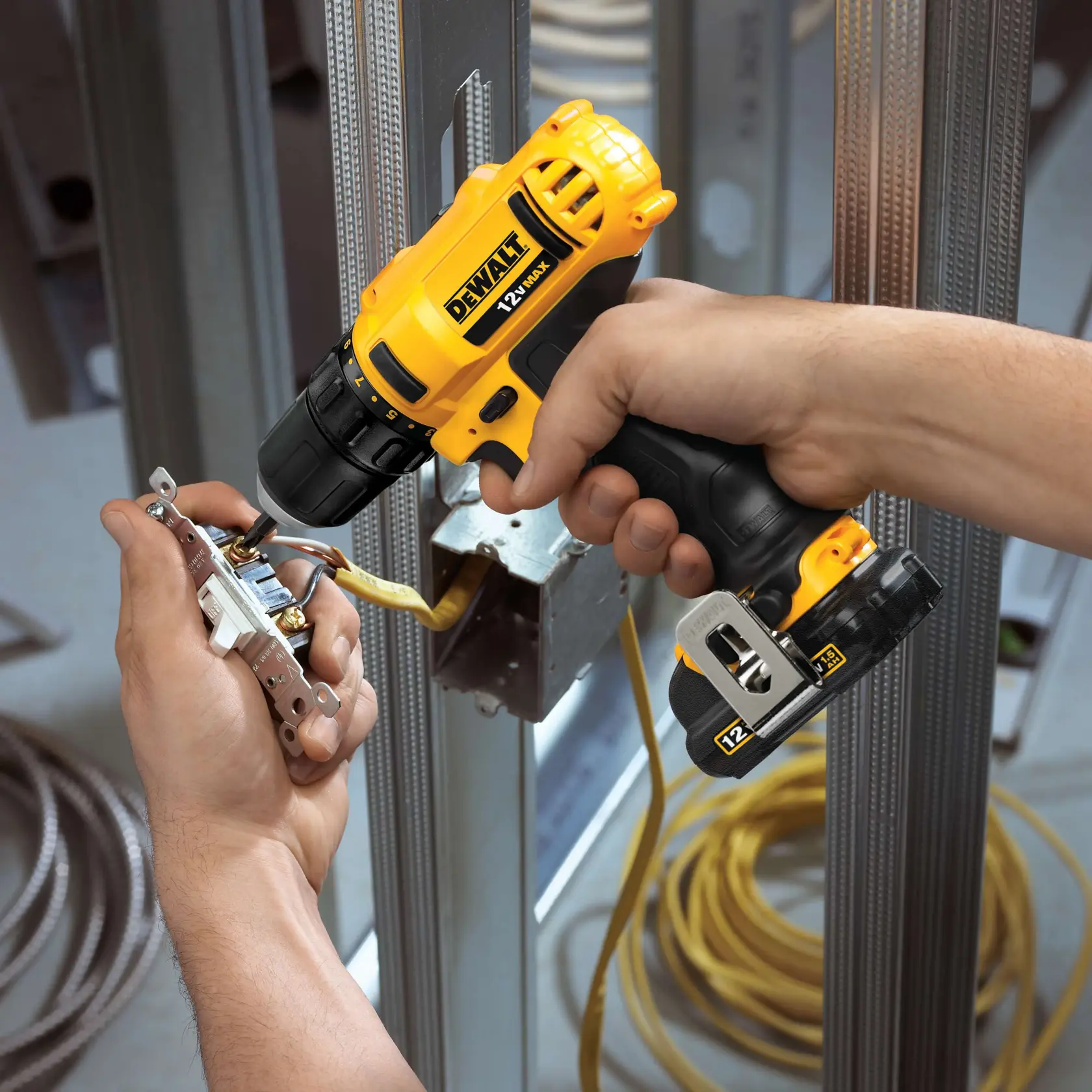 Una persona utiliza un taladro inalámbrico DEWALT de 12V para instalar componentes eléctricos en una caja metálica en un sitio de construcción.