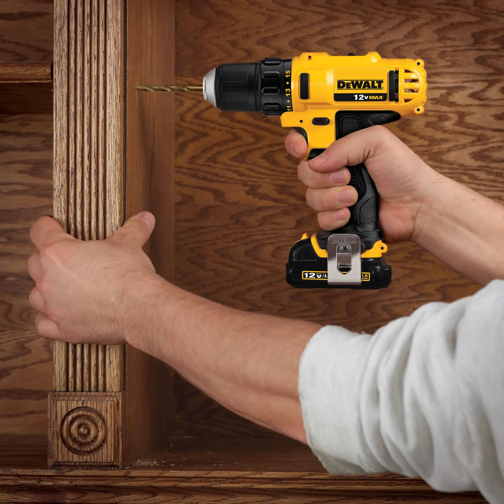 Una persona usando un taladro inalámbrico amarillo y negro DEWALT 12V MAX para perforar una estantería o gabinete de madera.