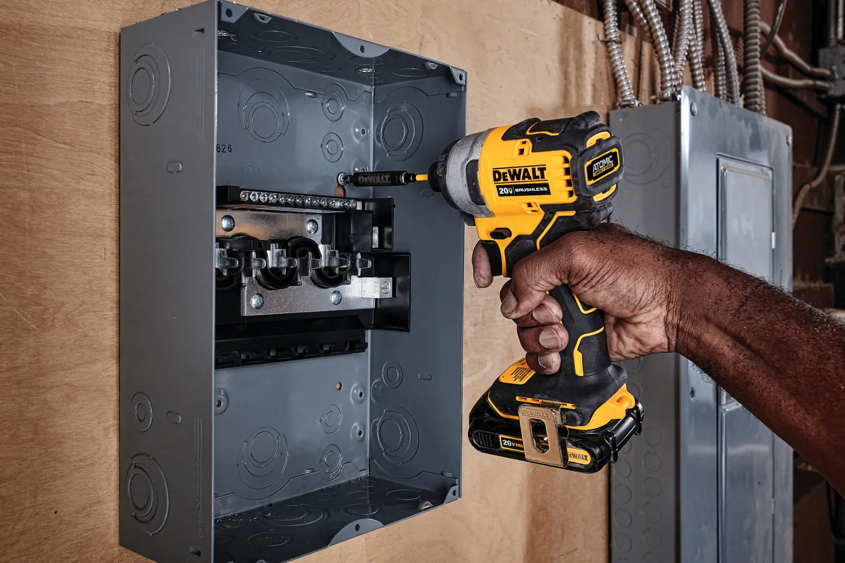 Una persona usando un destornillador de impacto inalámbrico DEWALT (modelo DCF809B) para trabajar dentro de un panel eléctrico montado en una pared.