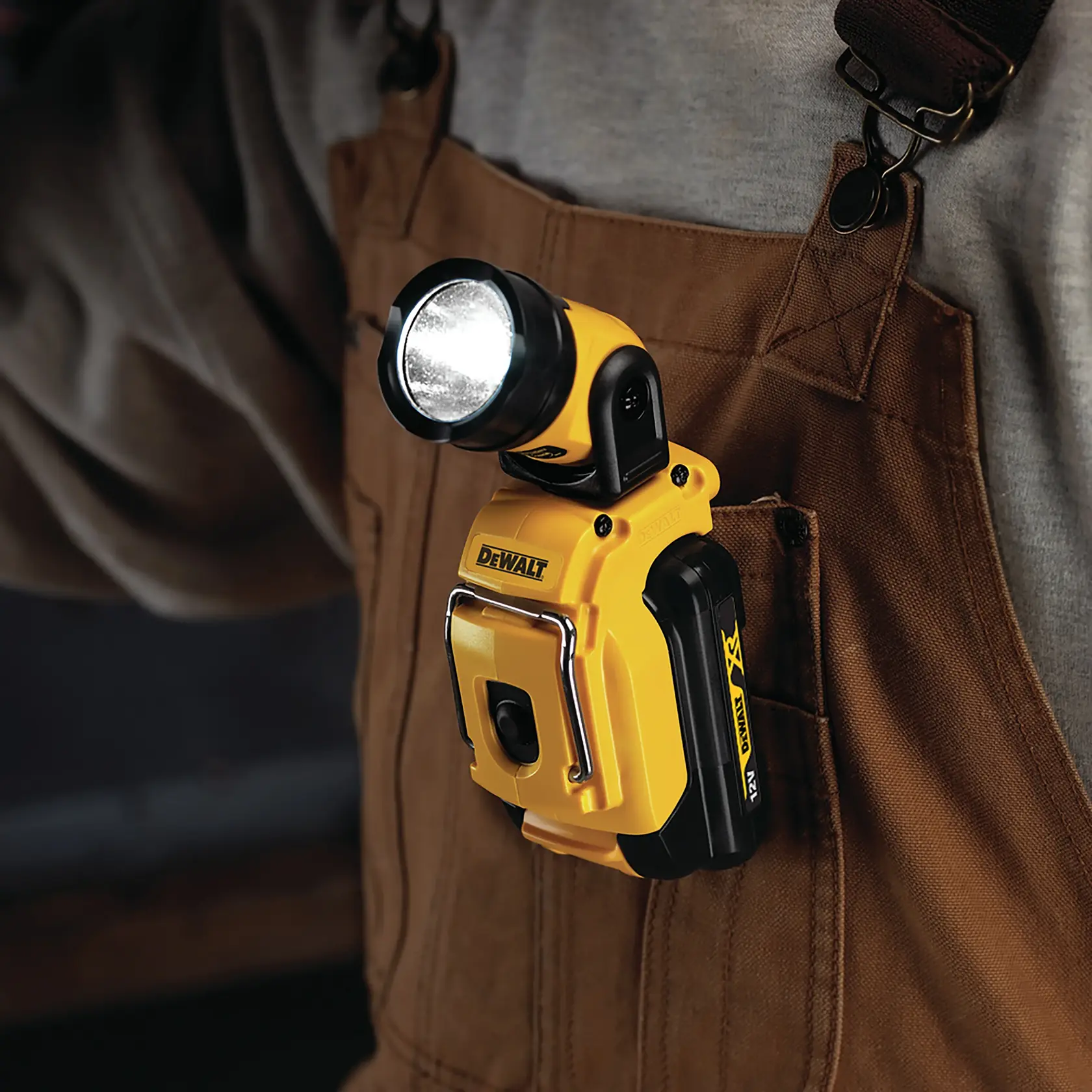 Luz de trabajo LED DEWALT DCL510 sujeta al bolsillo de un overol marrón, brillando.