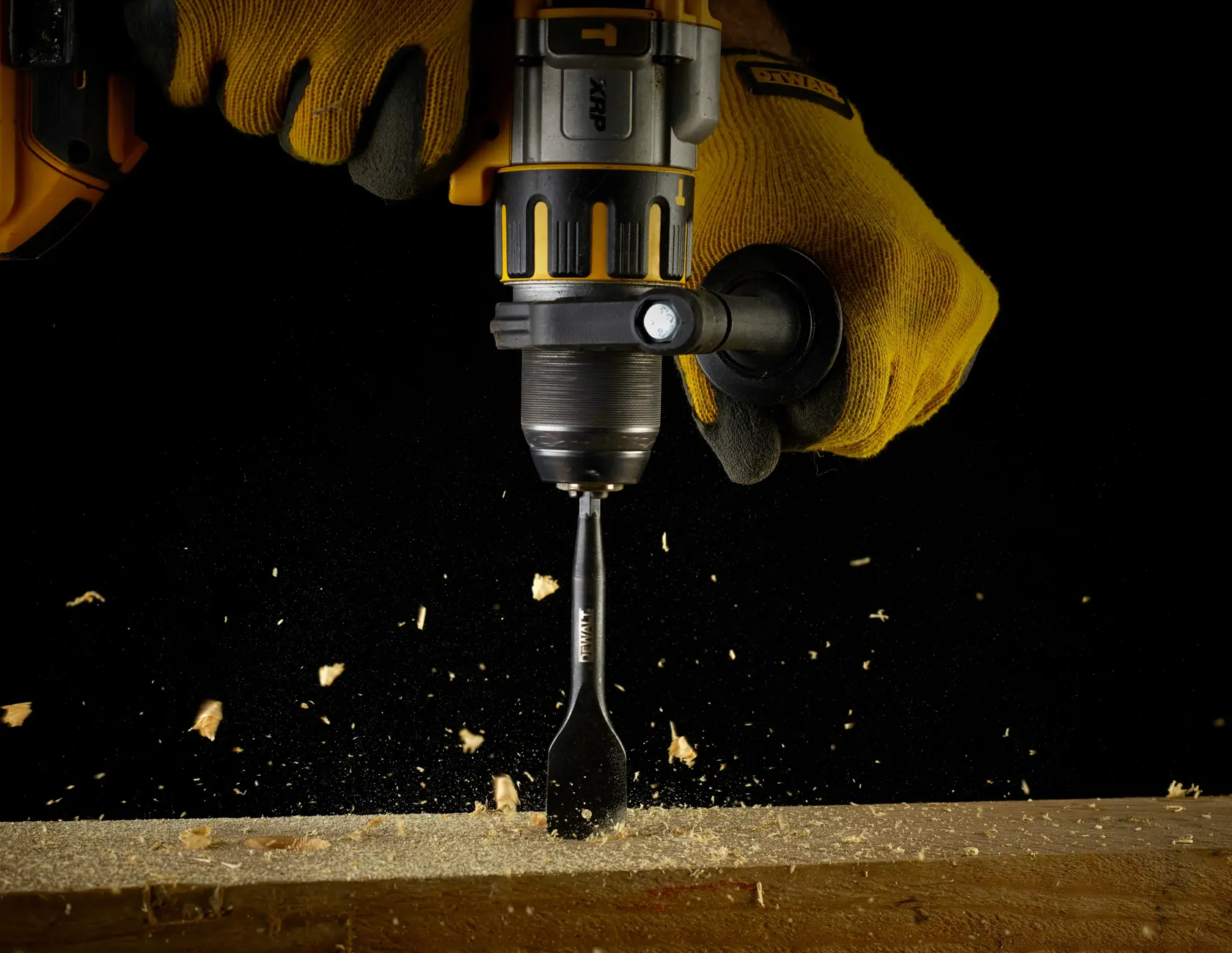 Taladro DEWALT con cincel trabaja en madera, crea chispas, sujetado por manos con guantes.