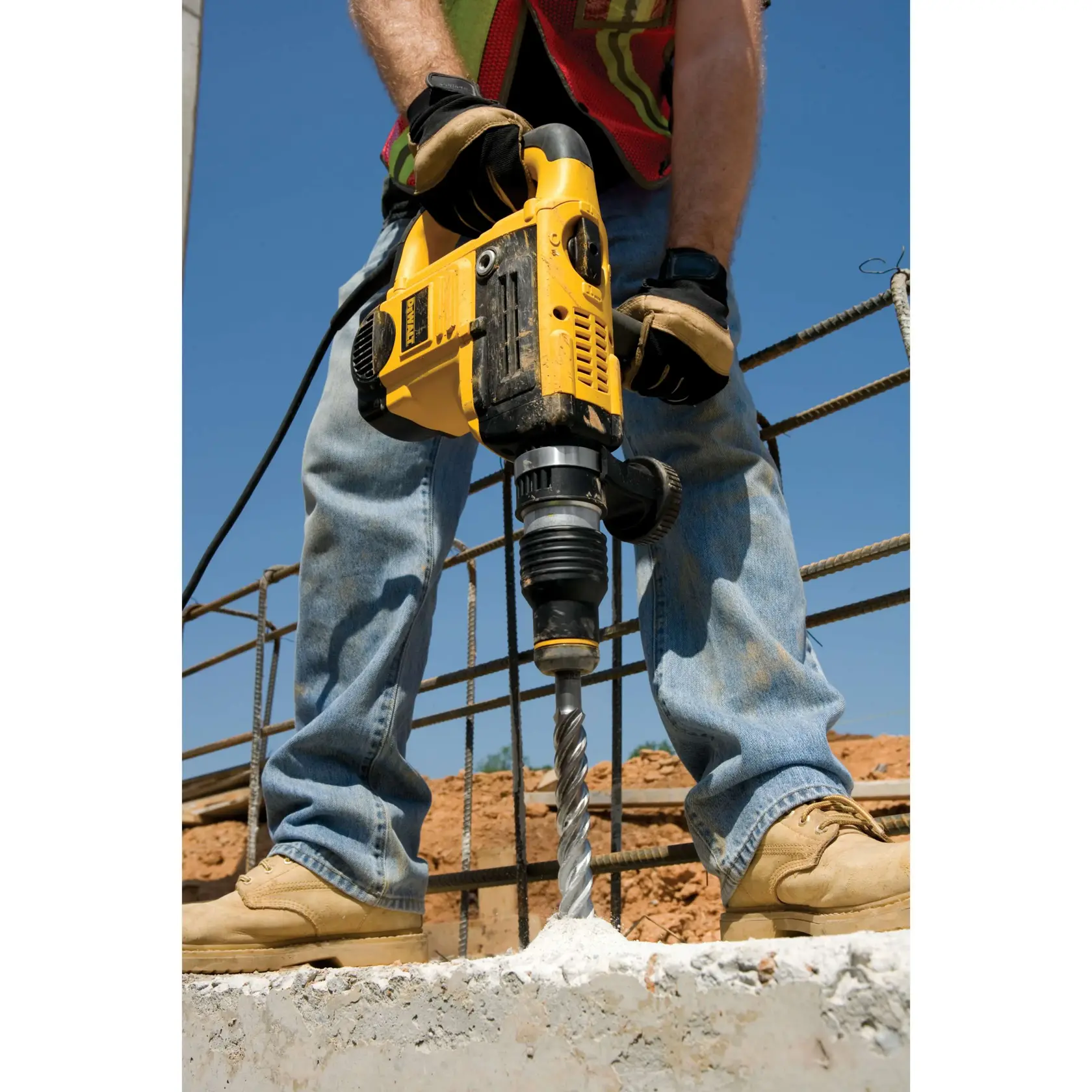 Trabajador perfora concreto con taladro martillo DEWALT en una obra exterior.