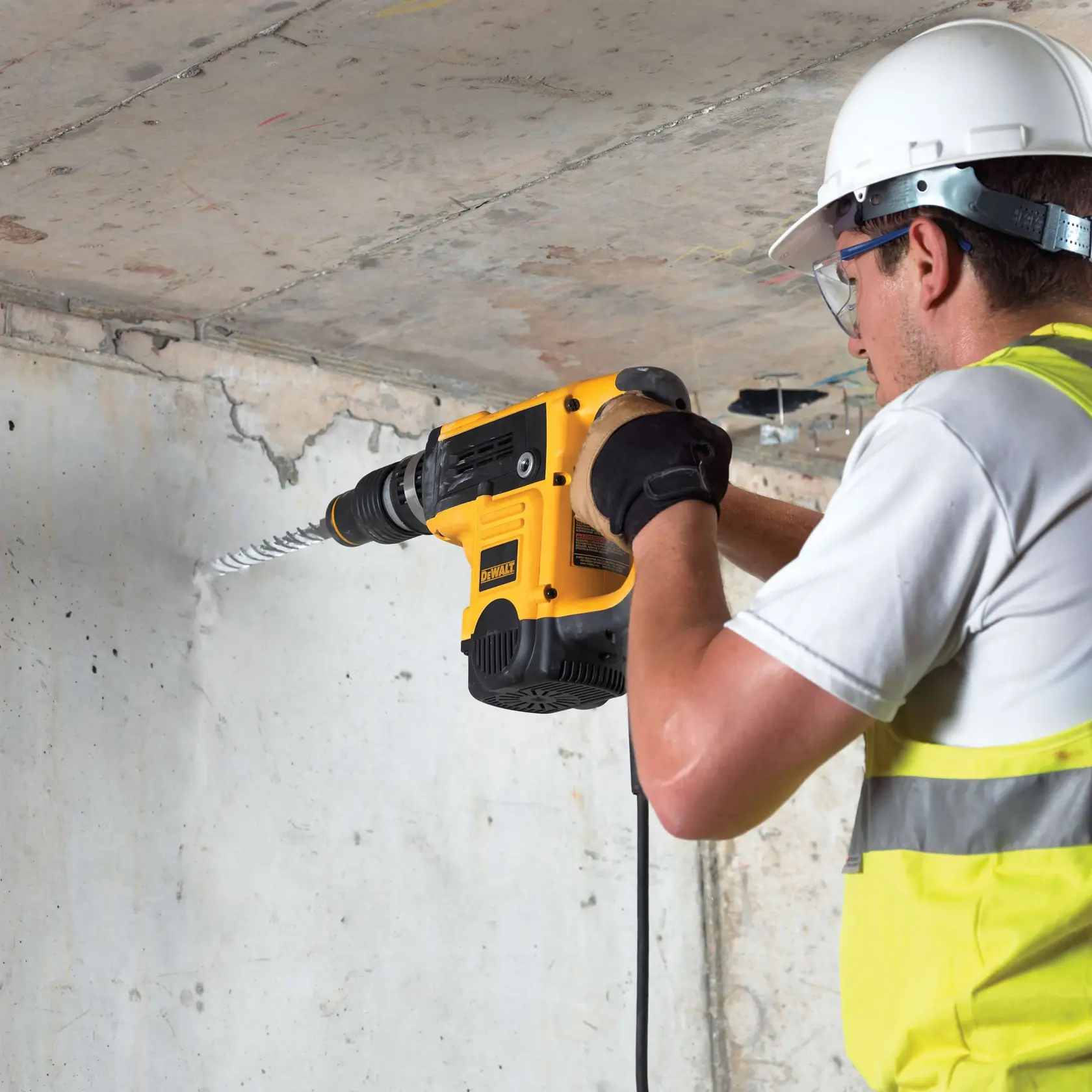 Persona perfora pared de concreto con martillo DEWALT y broca DT9442, usando equipo de seguridad.