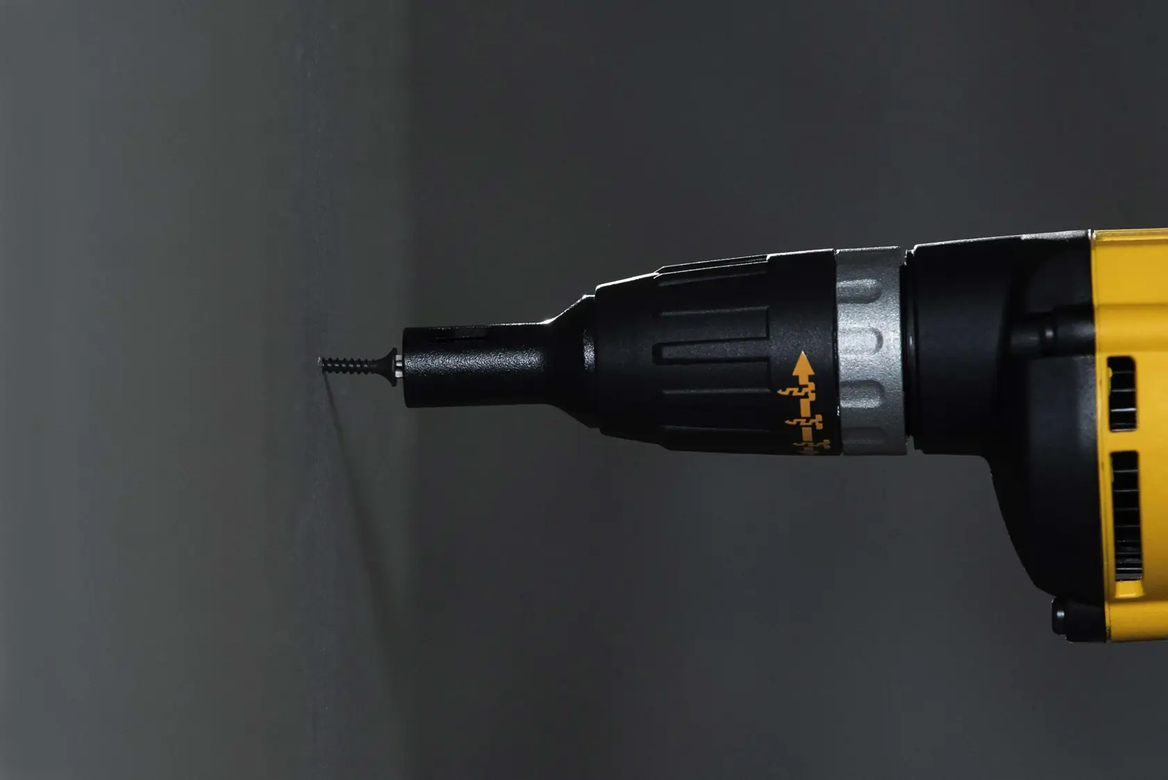 Imagen en primer plano de una herramienta eléctrica DEWALT amarilla y negra, específicamente un destornillador, atornillando un tornillo en una pared.