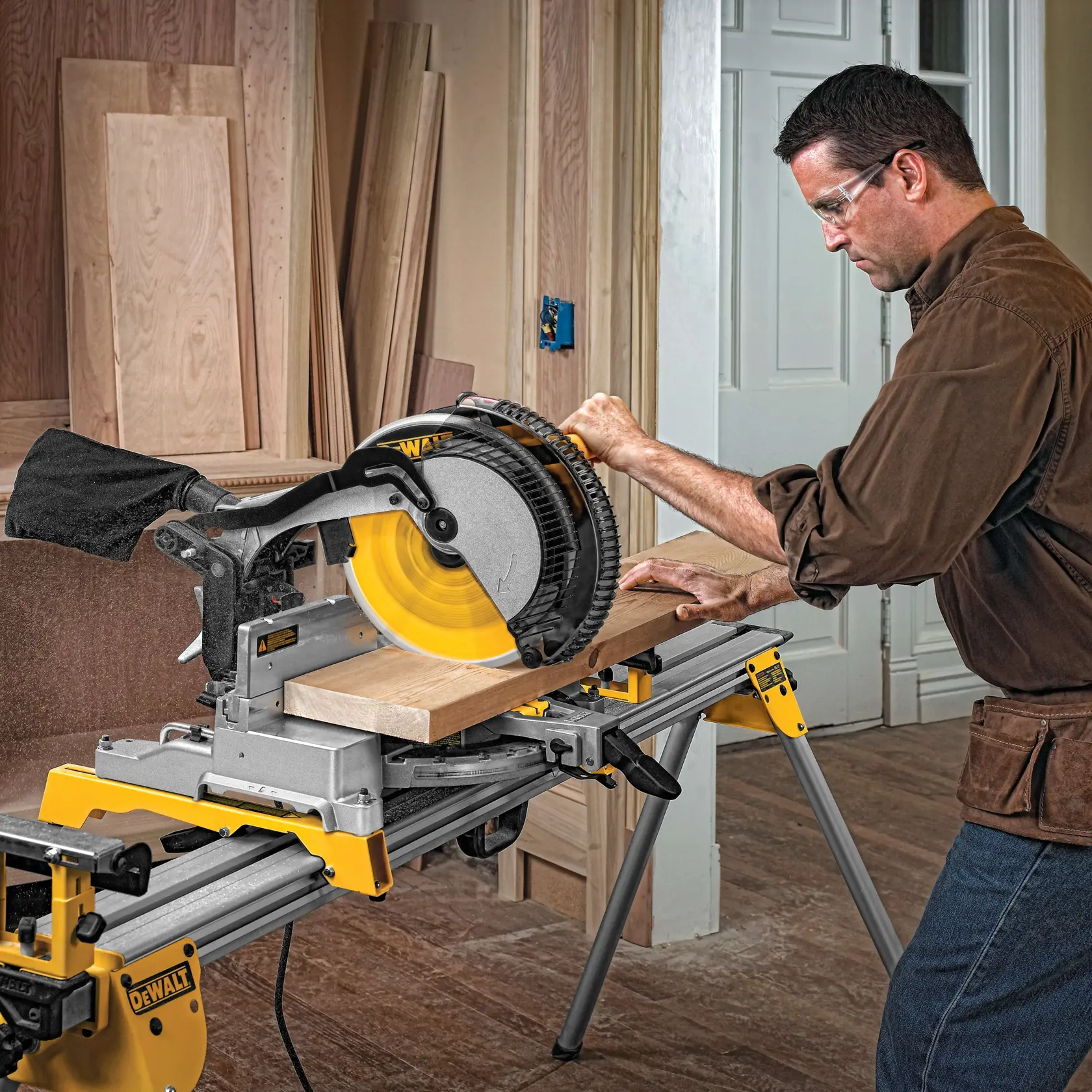 Una persona usa una sierra ingletadora DEWALT para cortar una tabla de madera en un taller interior, con varios paneles de madera en el fondo.
