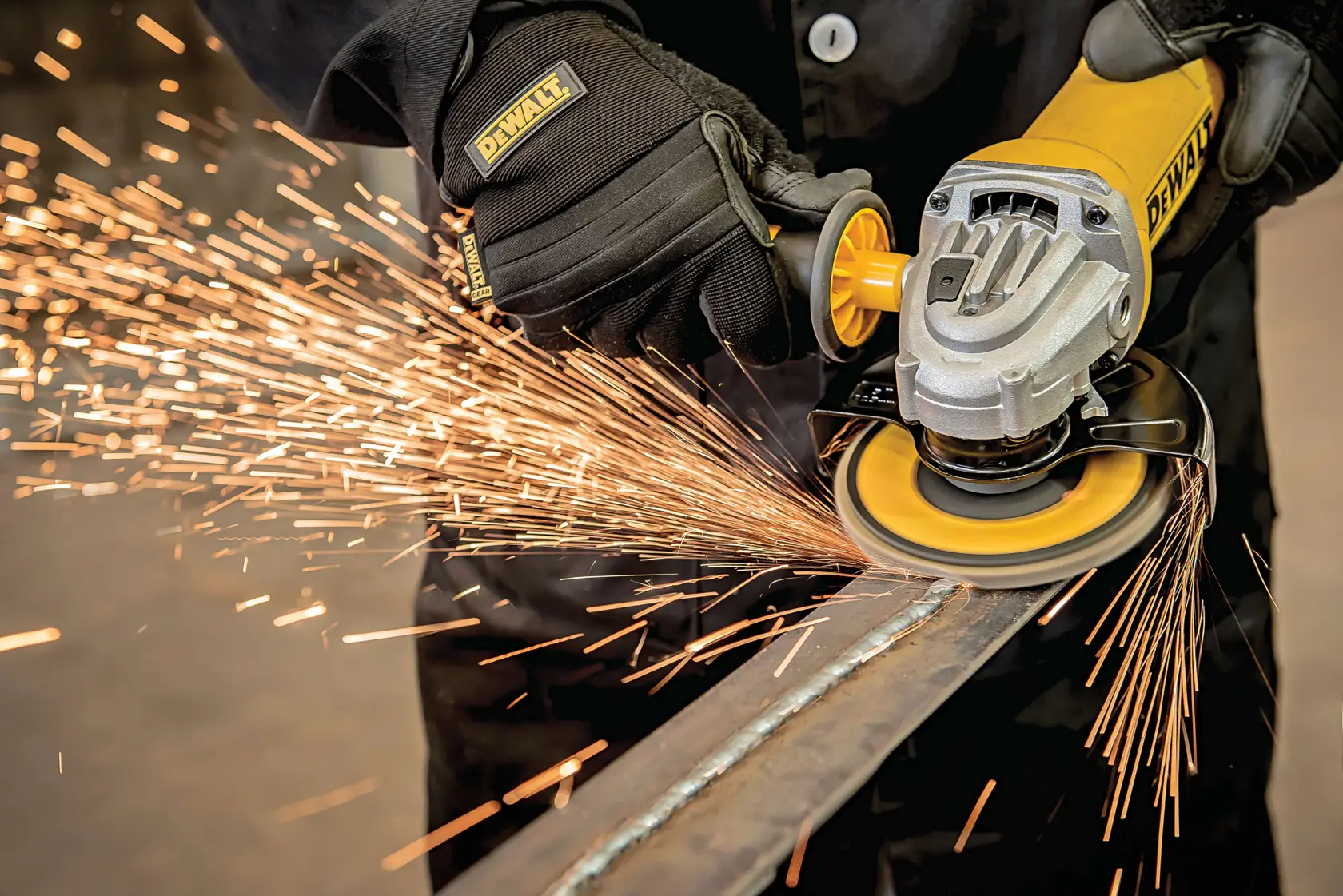Imagen en primer plano de una persona usando una amoladora angular DEWALT para trabajar una pieza de metal, con chispas brillantes que saltan mientras el instrumento opera. La persona lleva guantes y ropa protectora.