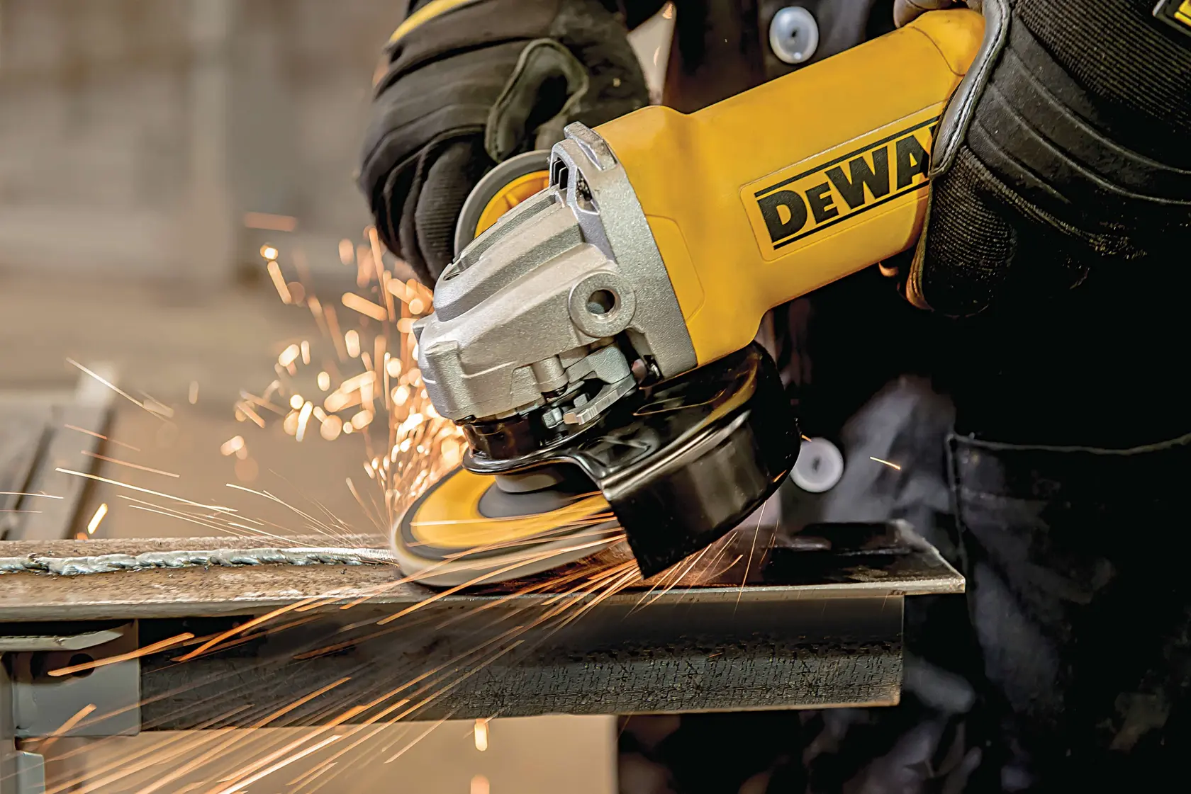 Primer plano de una persona con guantes usando una amoladora angular amarilla DEWALT para cortar metal, con chispas.