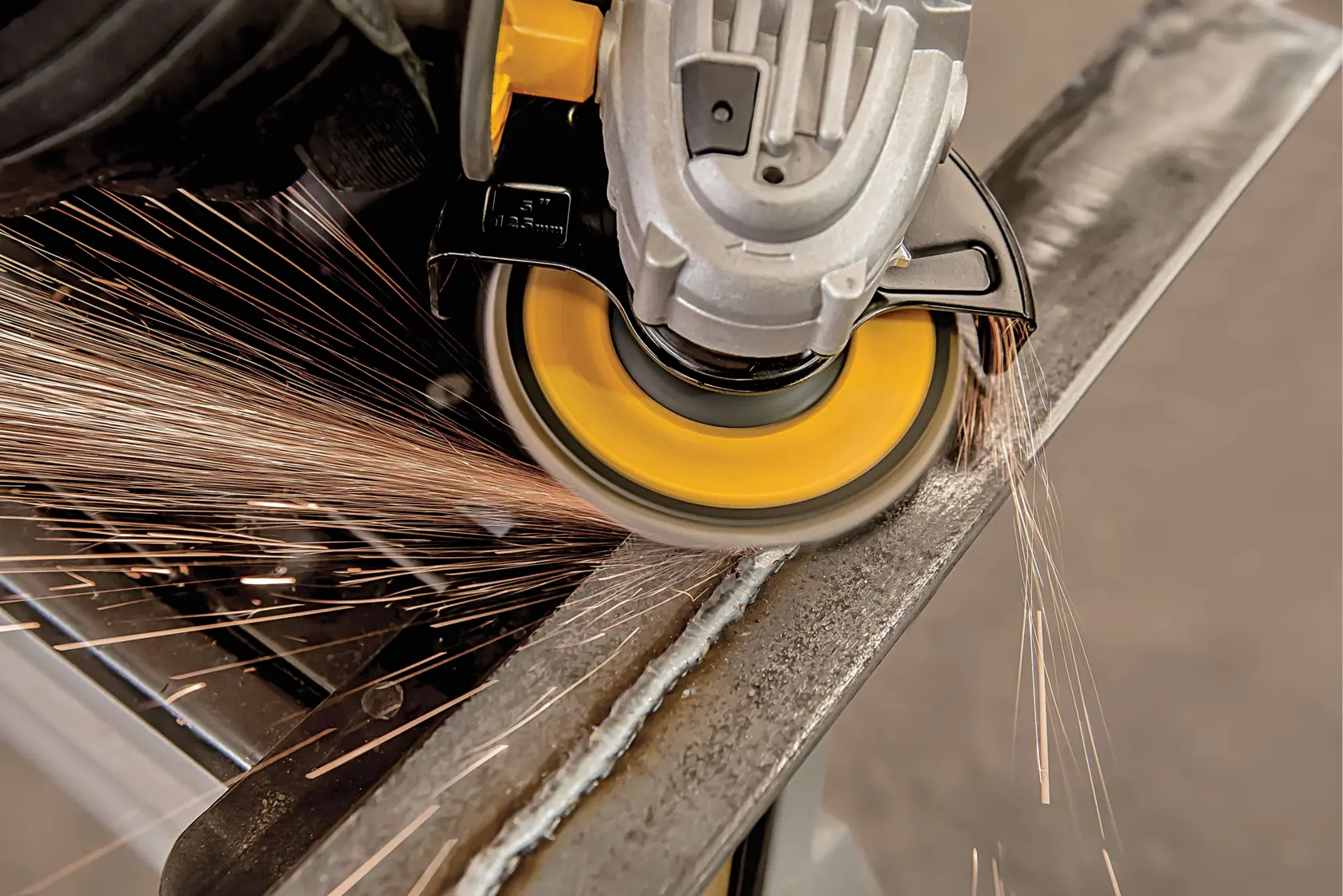 Primer plano de una amoladora angular DEWALT en funcionamiento, produciendo chispas mientras grinda el borde de una superficie metálica.