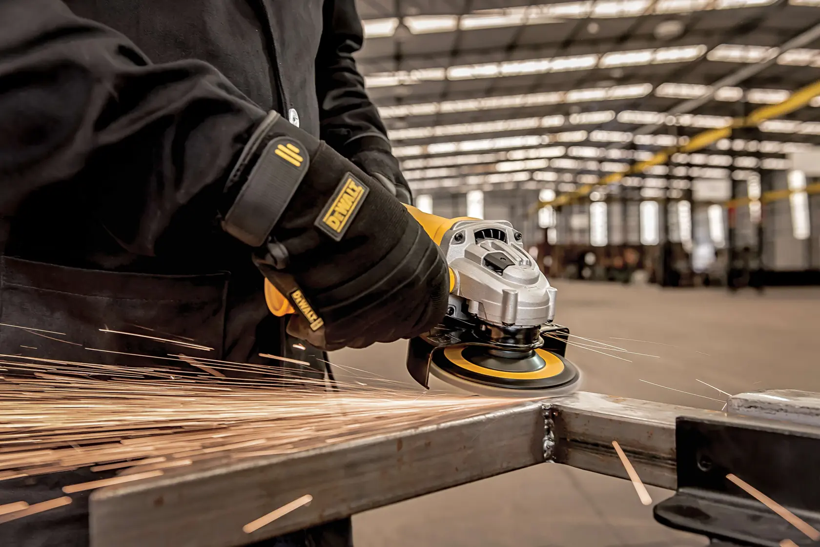 Vista en primer plano de una persona con guantes usando una amoladora angular DEWALT para alisar metal, con chispas volando en un taller industrial.