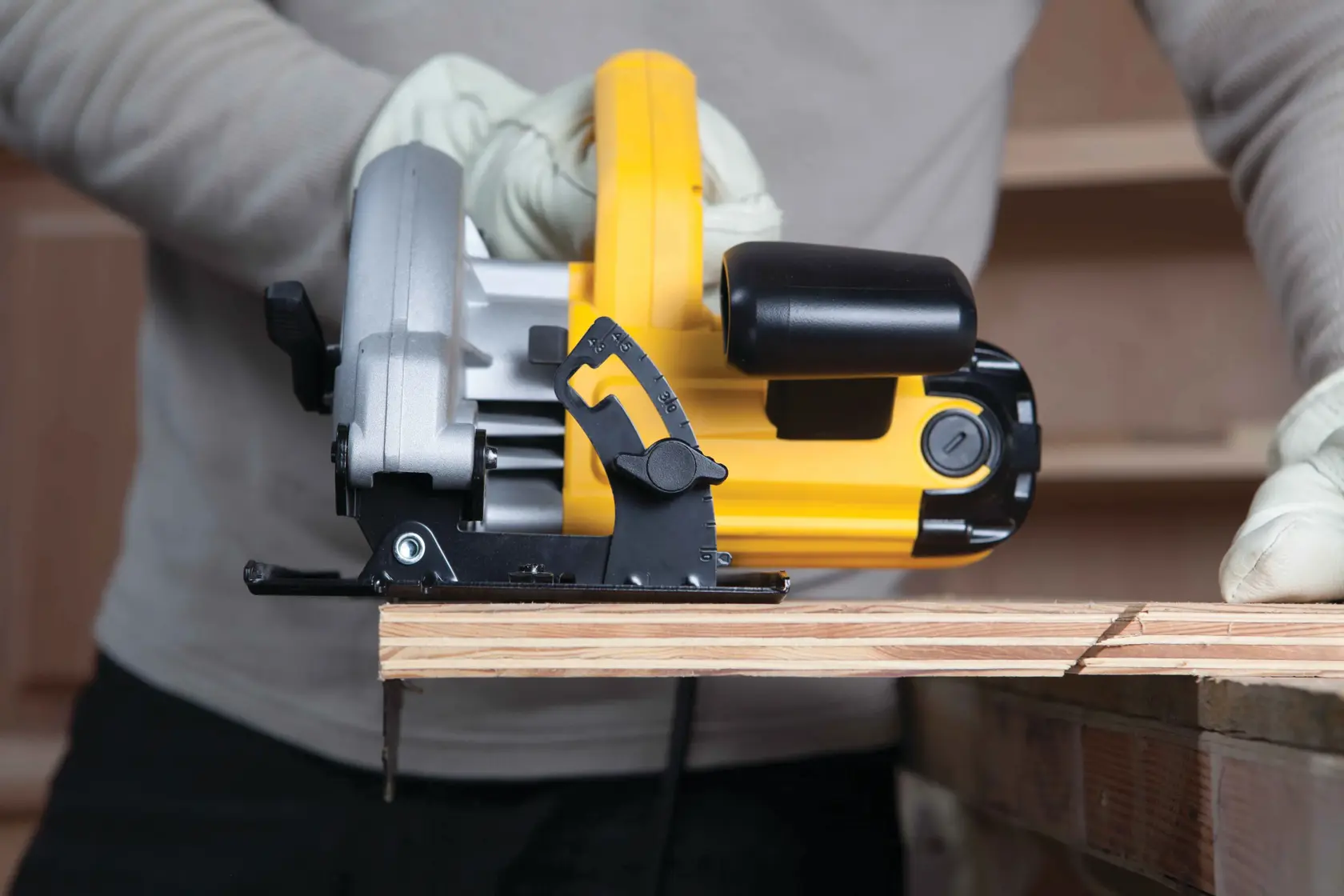 Una persona con guantes está usando una sierra circular DEWALT amarilla y negra para cortar un trozo de madera.